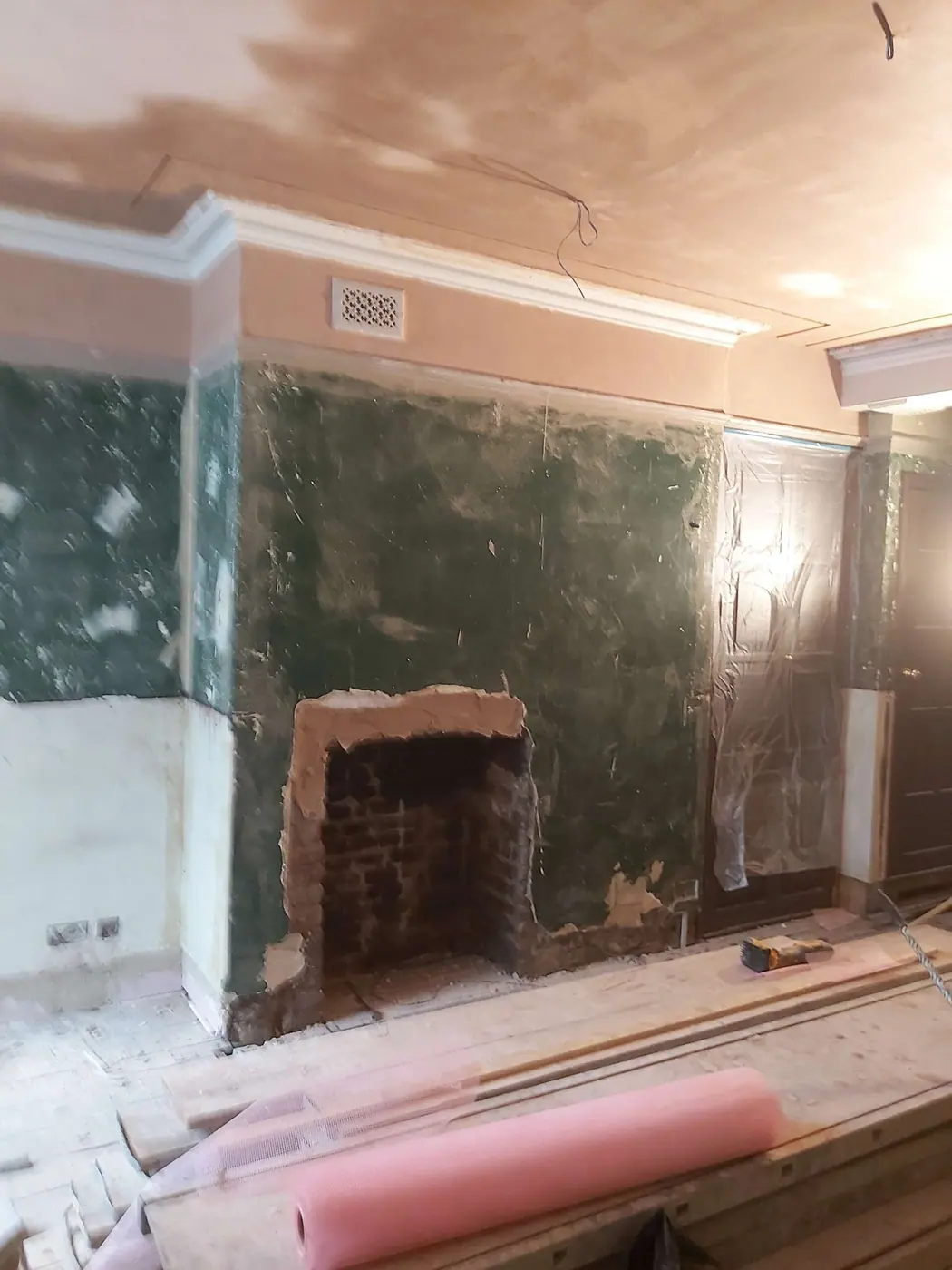 The showroom wall before, old plaster and green paint damaged around the fireplace